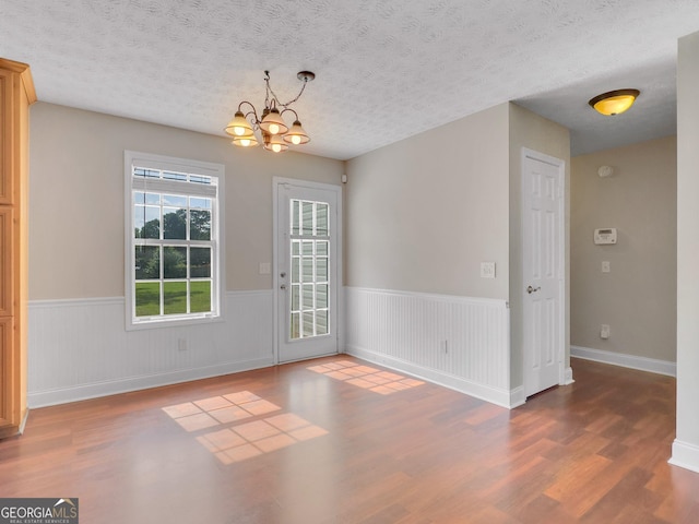 unfurnished dining area with dark wood-type flooring, a textured ceiling, and an inviting chandelier