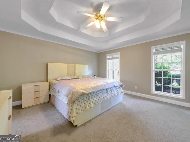 bedroom with light colored carpet, a raised ceiling, multiple windows, and ceiling fan