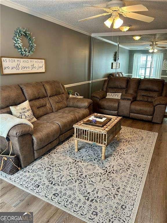 living room featuring wood-type flooring, a textured ceiling, and ornamental molding