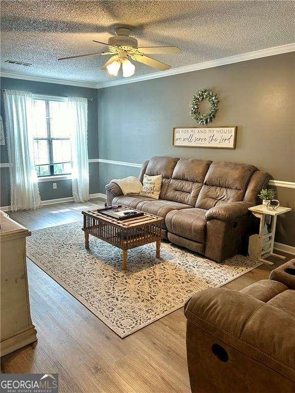 living room featuring ceiling fan, crown molding, wood-type flooring, and a textured ceiling