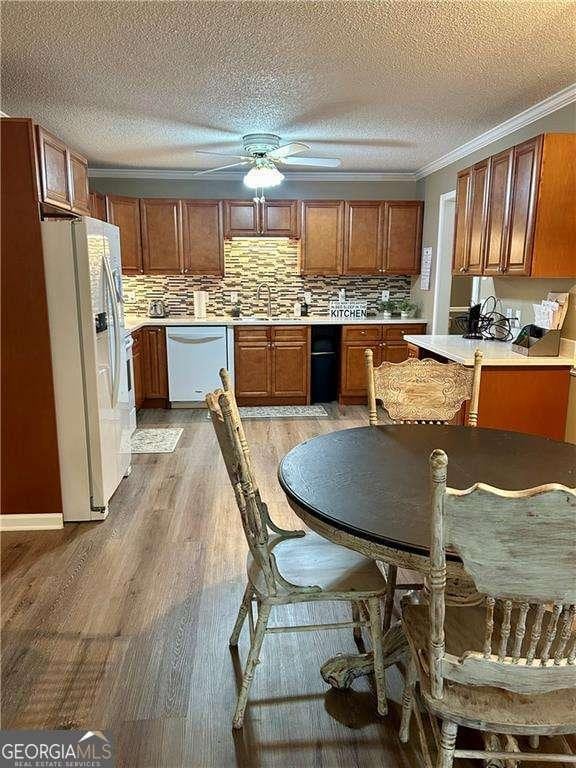 kitchen with dishwasher, white fridge with ice dispenser, tasteful backsplash, light hardwood / wood-style flooring, and crown molding