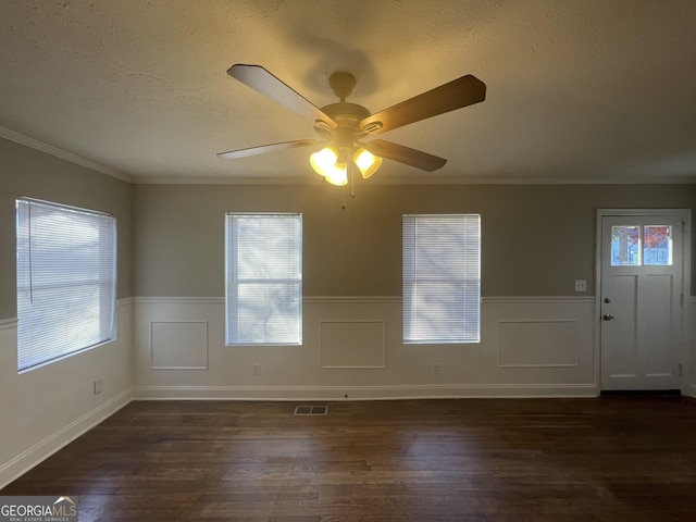 empty room featuring ornamental molding, ceiling fan, a wealth of natural light, and dark hardwood / wood-style floors