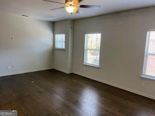 empty room featuring ceiling fan, dark wood-type flooring, and a wealth of natural light