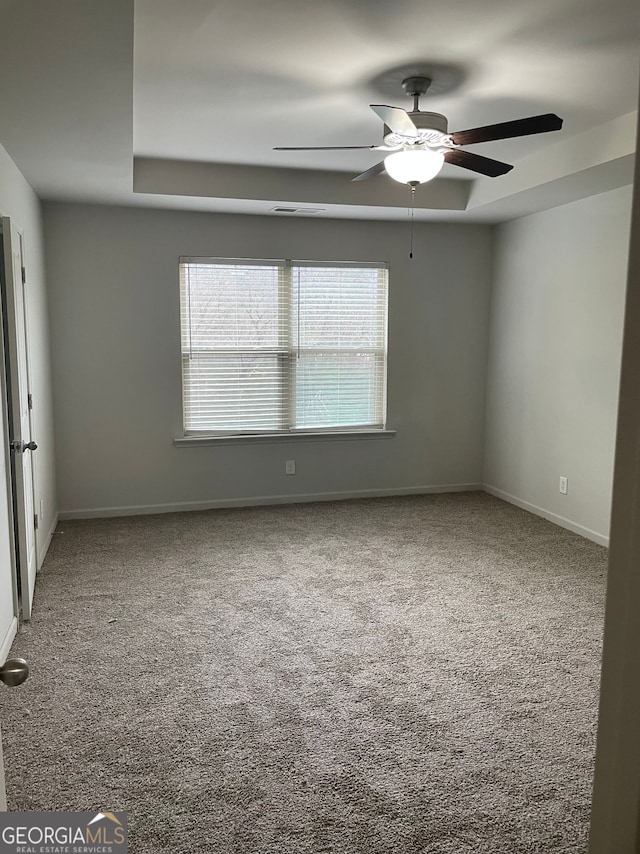 carpeted spare room featuring ceiling fan and a tray ceiling