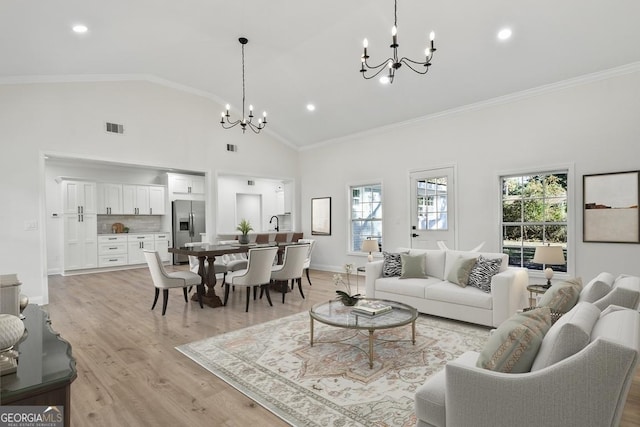 living room featuring ornamental molding, light hardwood / wood-style floors, high vaulted ceiling, and a notable chandelier