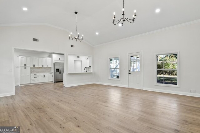 unfurnished living room with light wood-type flooring, an inviting chandelier, and ornamental molding