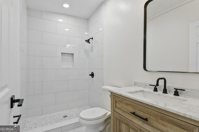 bathroom with tile patterned flooring, a tile shower, vanity, and toilet