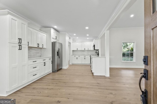 kitchen with white cabinetry, backsplash, stainless steel fridge, light hardwood / wood-style floors, and ornamental molding