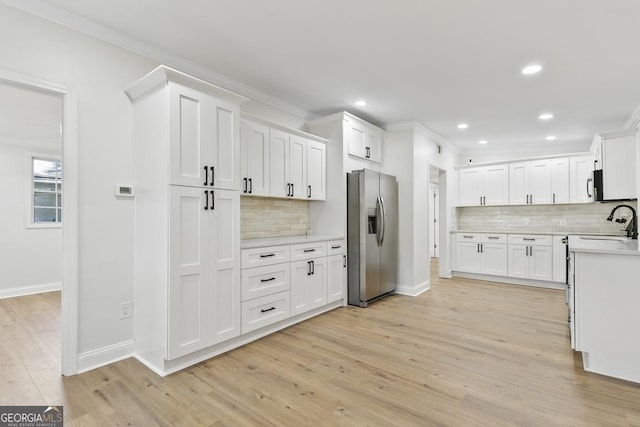 kitchen with white cabinets, crown molding, light wood-type flooring, and stainless steel appliances