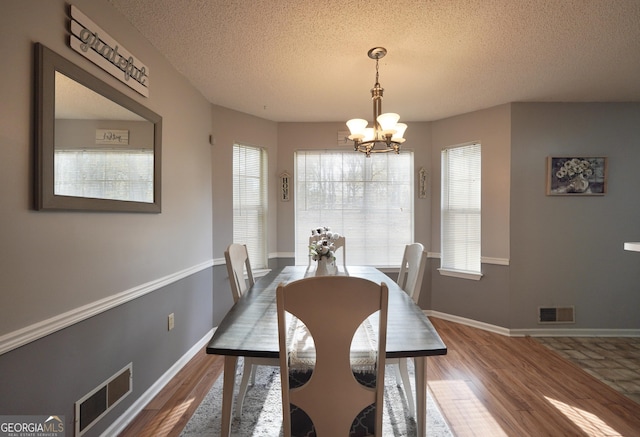 dining space with an inviting chandelier, a textured ceiling, and hardwood / wood-style flooring