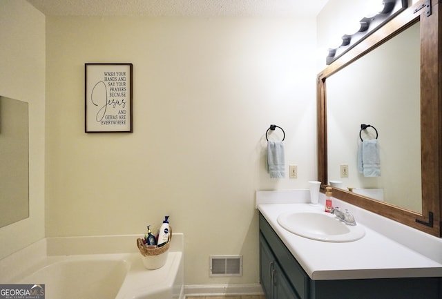 bathroom with a tub to relax in, vanity, and a textured ceiling