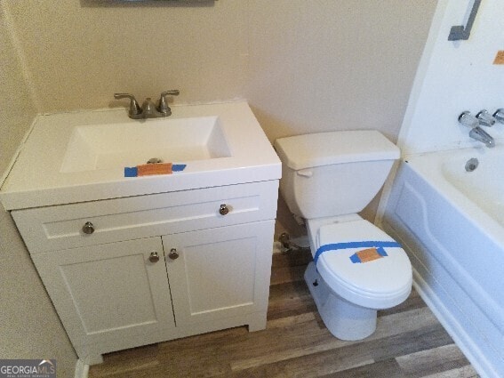 bathroom with toilet, a tub to relax in, wood finished floors, and vanity