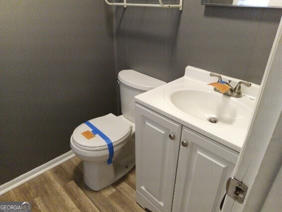 half bath featuring baseboards, vanity, toilet, and wood finished floors