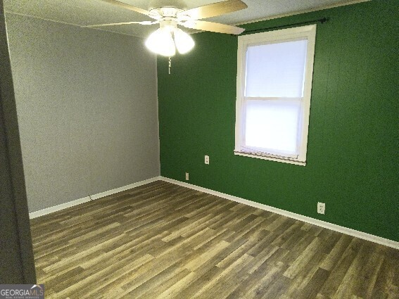 spare room featuring dark wood-style floors, ceiling fan, and baseboards