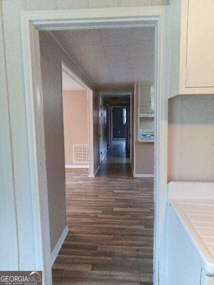 corridor with dark wood-style floors, visible vents, and baseboards