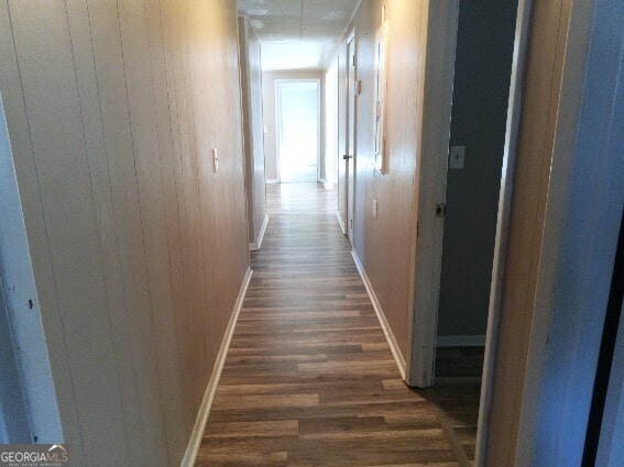 corridor with dark wood finished floors, wooden walls, and baseboards