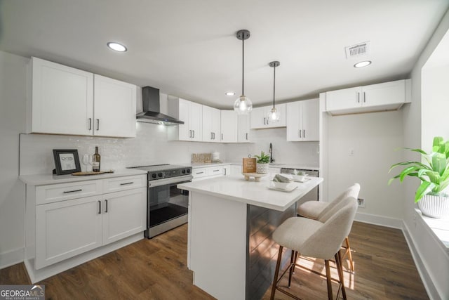 kitchen featuring stainless steel electric stove, decorative light fixtures, white cabinetry, and wall chimney range hood