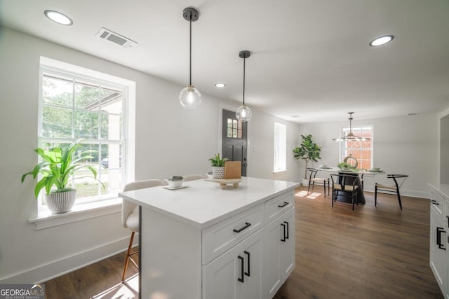 kitchen with a center island, a kitchen bar, white cabinets, hanging light fixtures, and dark hardwood / wood-style flooring