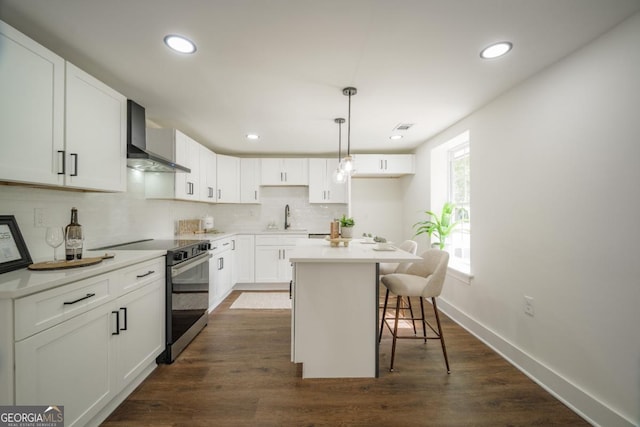 kitchen with a center island, electric stove, wall chimney range hood, decorative light fixtures, and white cabinetry