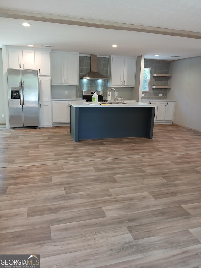 kitchen featuring a center island with sink, wall chimney range hood, sink, appliances with stainless steel finishes, and white cabinetry