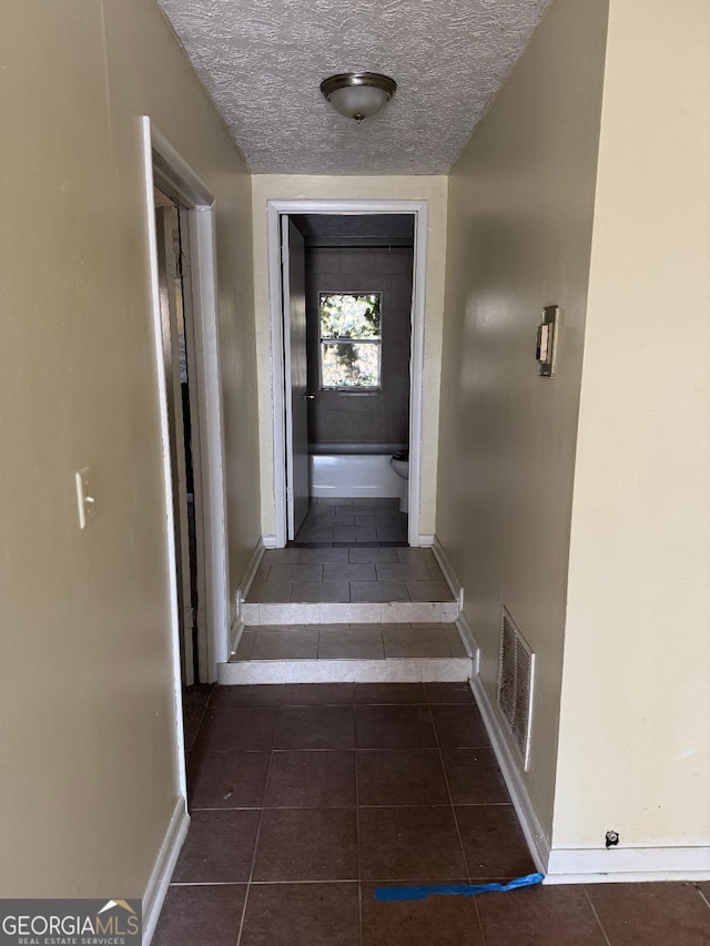 hall featuring a textured ceiling and dark tile patterned floors