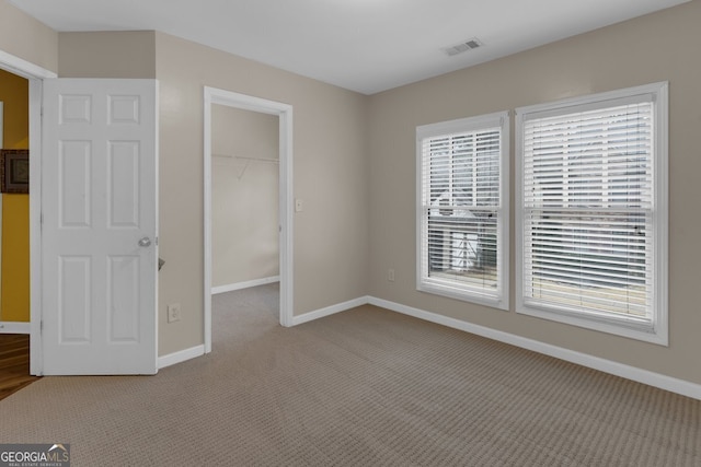 unfurnished bedroom with a closet, a walk in closet, light carpet, and multiple windows