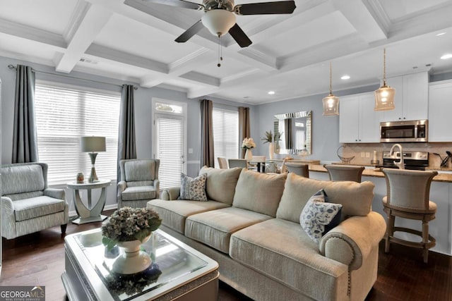 living room featuring dark wood-type flooring, beam ceiling, ornamental molding, ceiling fan, and coffered ceiling