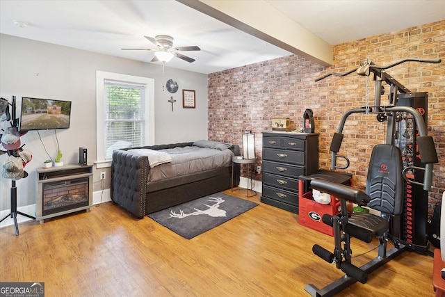 bedroom featuring beam ceiling, ceiling fan, hardwood / wood-style floors, and brick wall