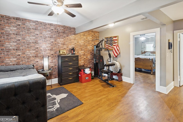 bedroom featuring beamed ceiling, light wood-type flooring, ceiling fan, and brick wall