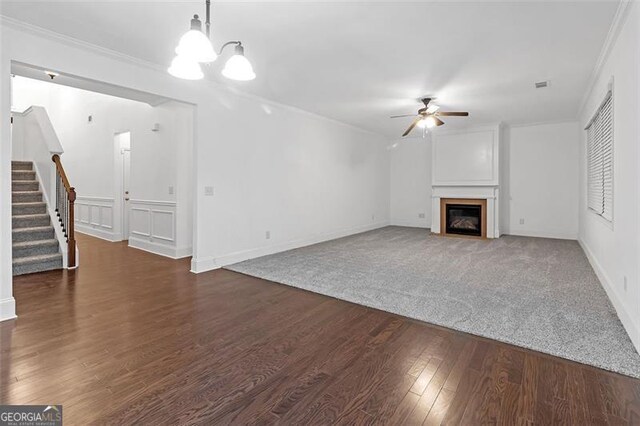 unfurnished living room featuring ceiling fan with notable chandelier, dark hardwood / wood-style flooring, and ornamental molding