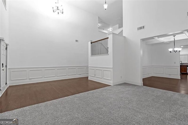 spare room with a chandelier, a towering ceiling, and dark carpet