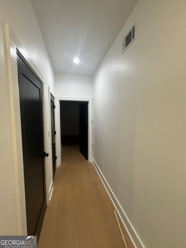 corridor featuring baseboards, light wood-style floors, and visible vents
