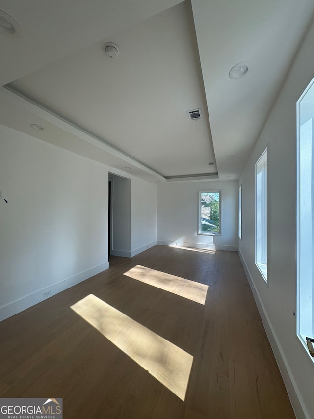 unfurnished room with baseboards, a tray ceiling, visible vents, and dark wood finished floors