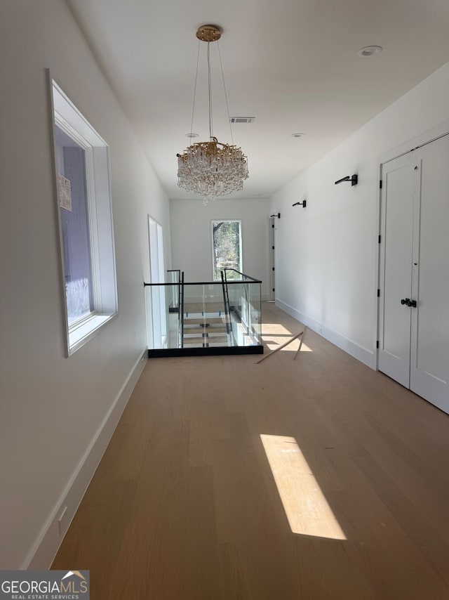 hallway featuring an inviting chandelier, wood finished floors, baseboards, and visible vents