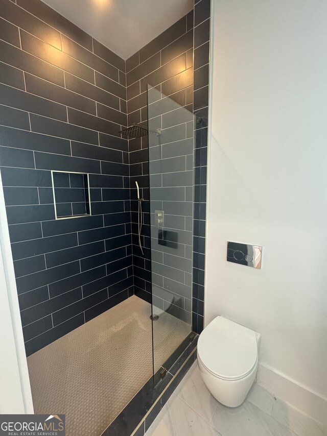 bathroom featuring marble finish floor, baseboards, a tile shower, and toilet