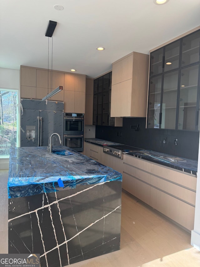 kitchen with modern cabinets, a sink, multiple ovens, pendant lighting, and backsplash