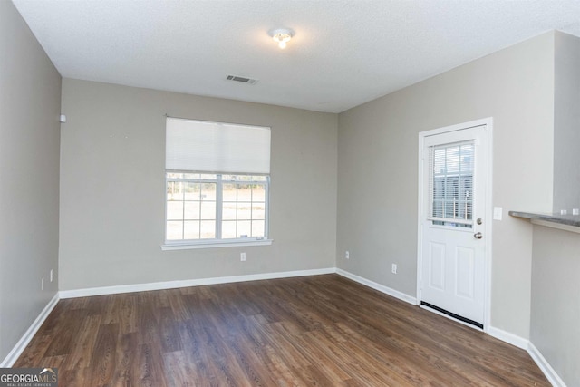 spare room featuring dark hardwood / wood-style floors, a textured ceiling, and a wealth of natural light