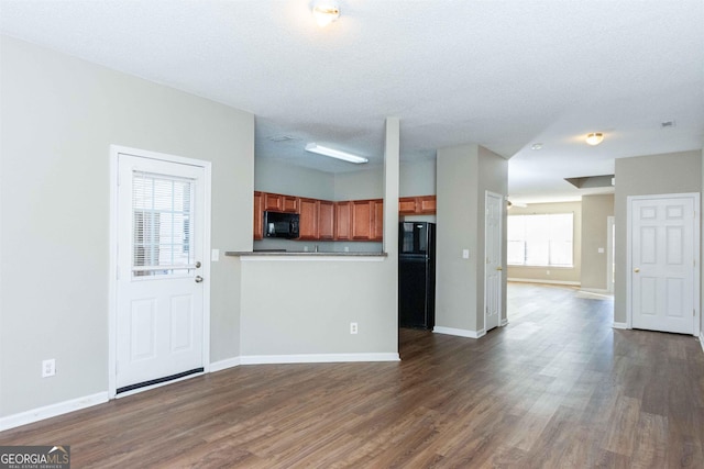 kitchen with a textured ceiling, kitchen peninsula, black appliances, and dark hardwood / wood-style floors