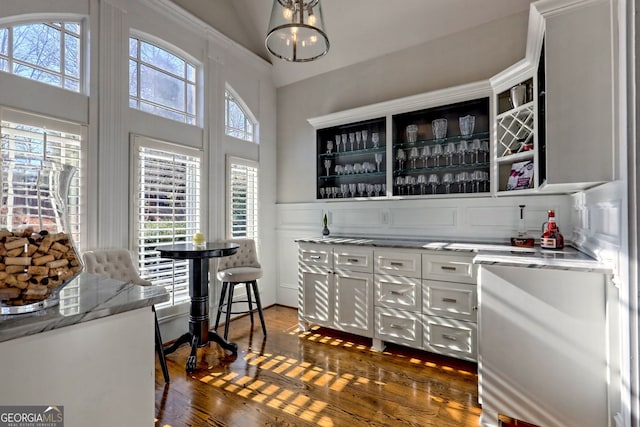 bar with dark wood-type flooring, white cabinetry, a chandelier, and light stone countertops