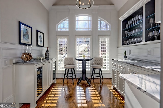 bar with light stone counters, white cabinets, dark hardwood / wood-style floors, and lofted ceiling