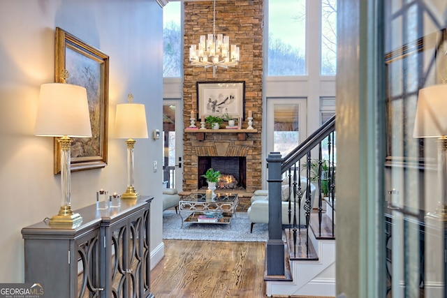 foyer featuring a high ceiling, a stone fireplace, an inviting chandelier, and wood-type flooring