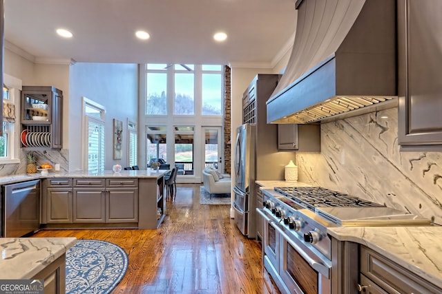 kitchen featuring light stone countertops, custom exhaust hood, tasteful backsplash, and appliances with stainless steel finishes