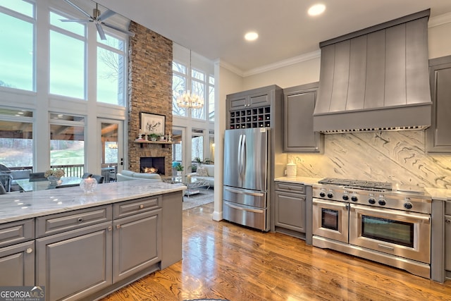 kitchen featuring stainless steel appliances, gray cabinetry, custom range hood, and a stone fireplace