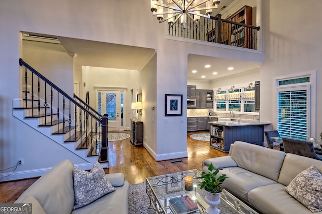 living room with a towering ceiling, crown molding, a notable chandelier, dark hardwood / wood-style flooring, and sink