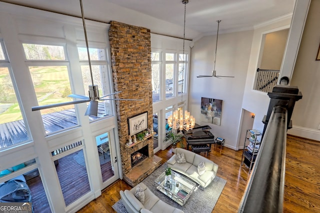 living room featuring hardwood / wood-style flooring, ornamental molding, a towering ceiling, a fireplace, and ceiling fan