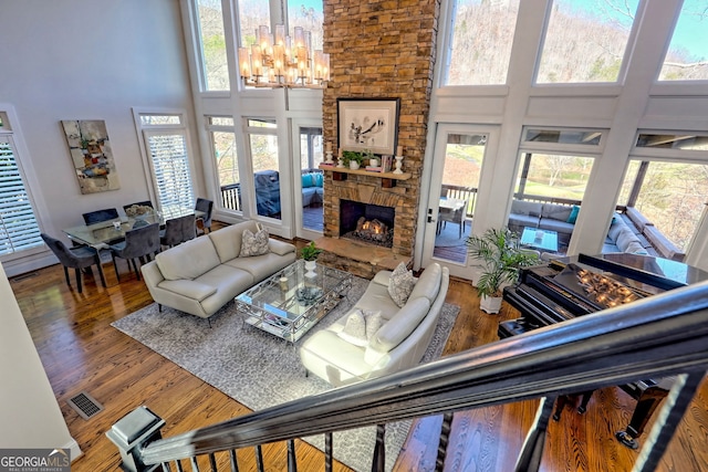 living room featuring a high ceiling, a stone fireplace, an inviting chandelier, and hardwood / wood-style flooring