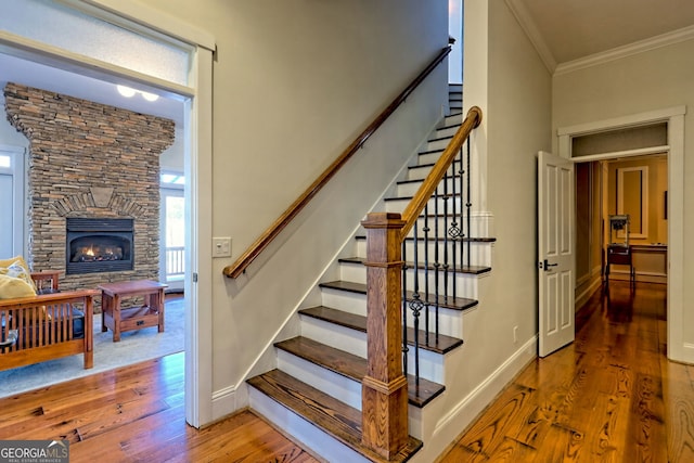 stairs featuring hardwood / wood-style flooring, crown molding, and a stone fireplace