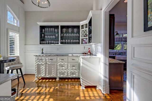 bar with light stone counters, dark wood-type flooring, and white cabinetry