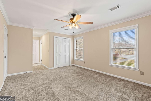 unfurnished bedroom featuring ceiling fan, a closet, crown molding, and light colored carpet