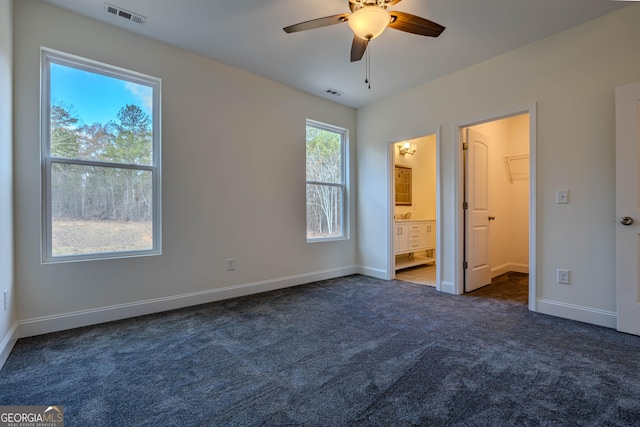 unfurnished bedroom with dark colored carpet, ensuite bathroom, and ceiling fan